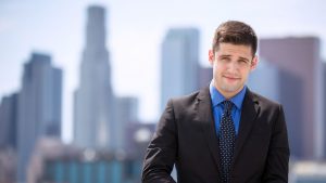 Young man wearing a suit standing outside with a city skyline in the background