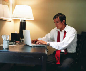 Man sitting at desk with tie draped around his neck. looking fatigued returning to work after a long holiday weekend.
