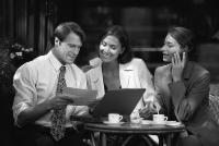 Business professionals discussing healthcare staffing strategies at a café, reviewing documents and using a laptop.
