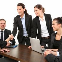 Healthcare professionals demonstrating soft skills during team meeting: active listening, collaboration, and engaged communication displayed as business-attired team members interact around laptop in conference setting, exemplifying interprofessional dynamics in medical administration.